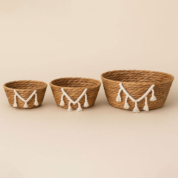Three woven baskets with decorative tassels on a beige background