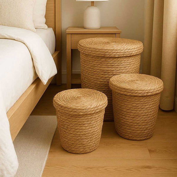 Three woven baskets on a wooden floor next to a bed in a bedroom setting.