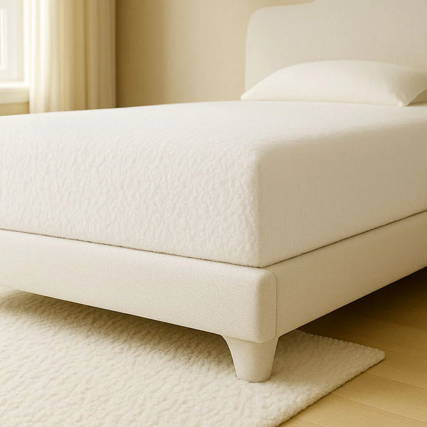 White waterproof cotton mattress protector fitted on a bed in a softly lit, minimalist bedroom