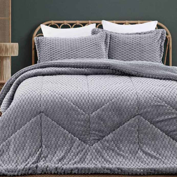 Gray quilted comforter on a bed with white pillows against a dark wall.