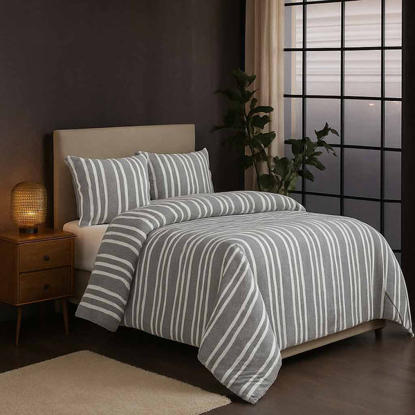 Striped winter comforter set on a bed in a dimly lit bedroom with a side table and lamp. 
