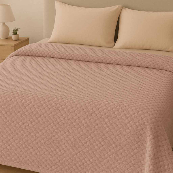 Bed with pink textured blanket and pillows in a bedroom setting