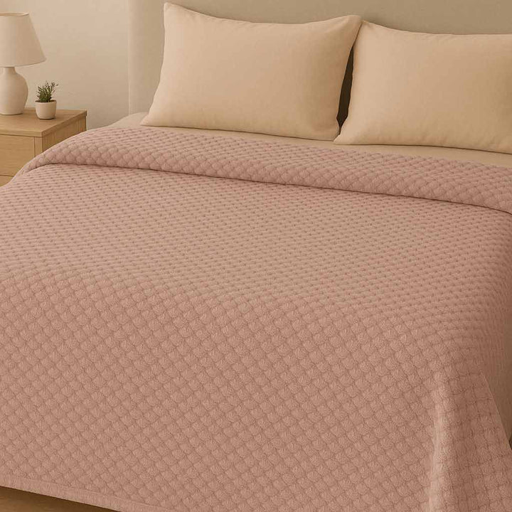 Bed with pink textured blanket and pillows in a bedroom setting