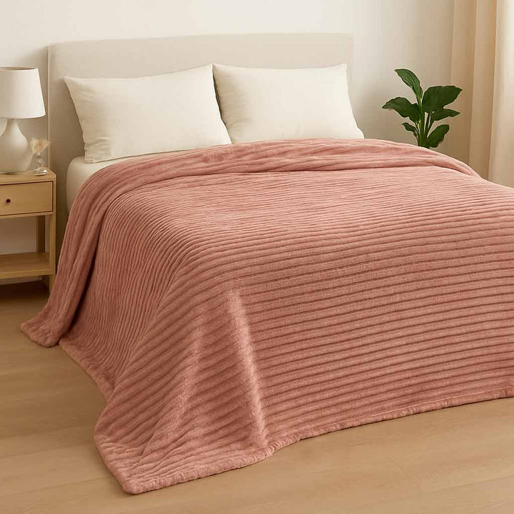 Pink blanket draped over a bed in a bedroom setting with a lamp and plant.