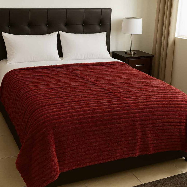 Bed with a deep red blanket, white pillows, and a nightstand with a lamp in a bedroom setting.