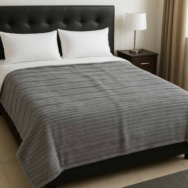 Gray textured blanket on a bed with a black headboard and nightstand in a bedroom setting.