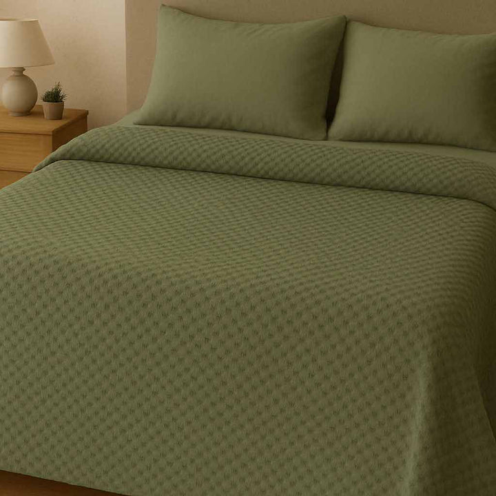 Green blanket and pillows on a bed in a bedroom setting.