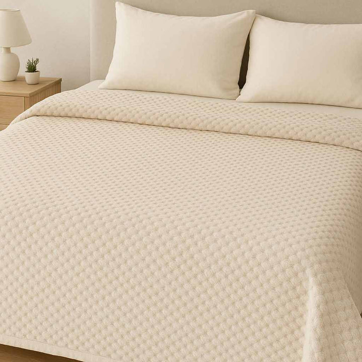 Off-White quilted blanket on a bed with pillows in a bedroom setting.