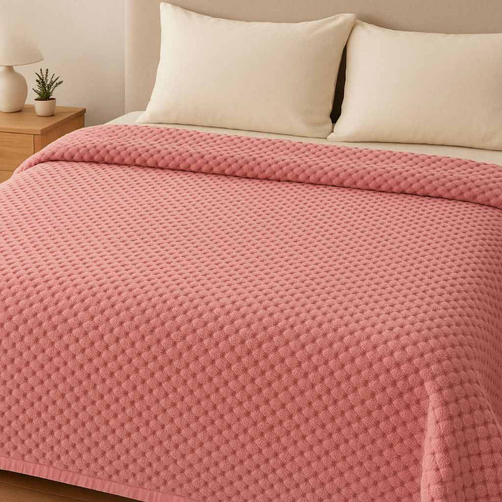 Pink textured blanket on a bed with white pillows and a nightstand.