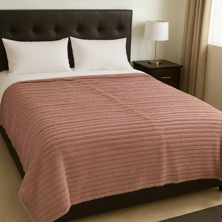 Bed with pink blanket and white pillows in a bedroom setting.
